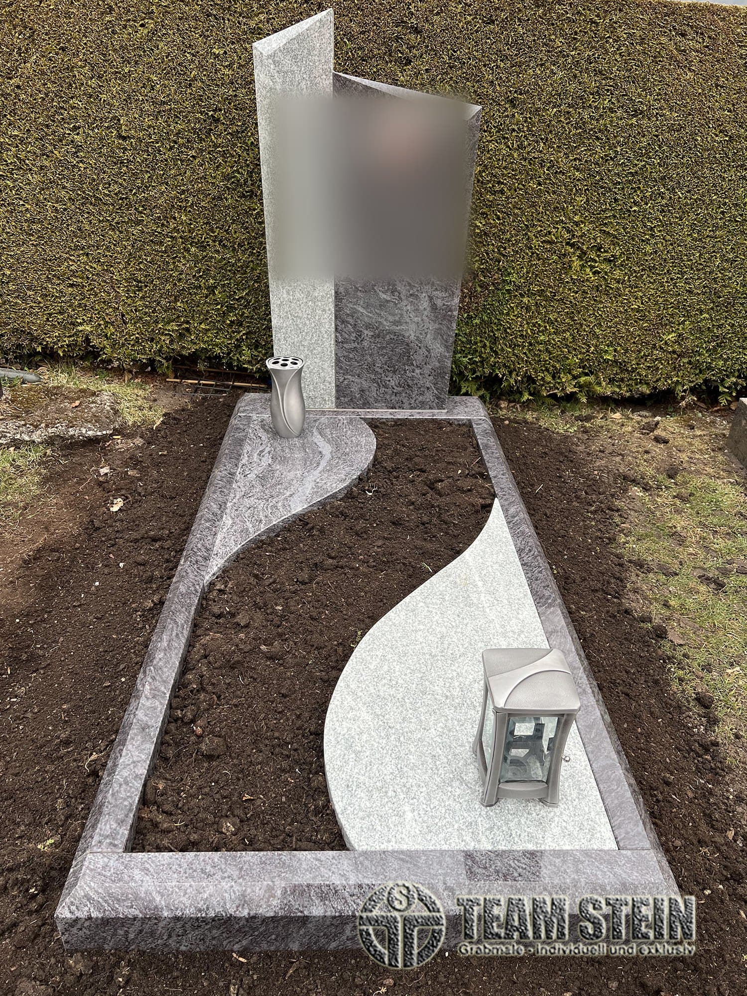 Zweiteilige Stele aus hellem und dunklem Stein, Einfassung mit hellem, geschwungenem Feld, Vase und Laterne